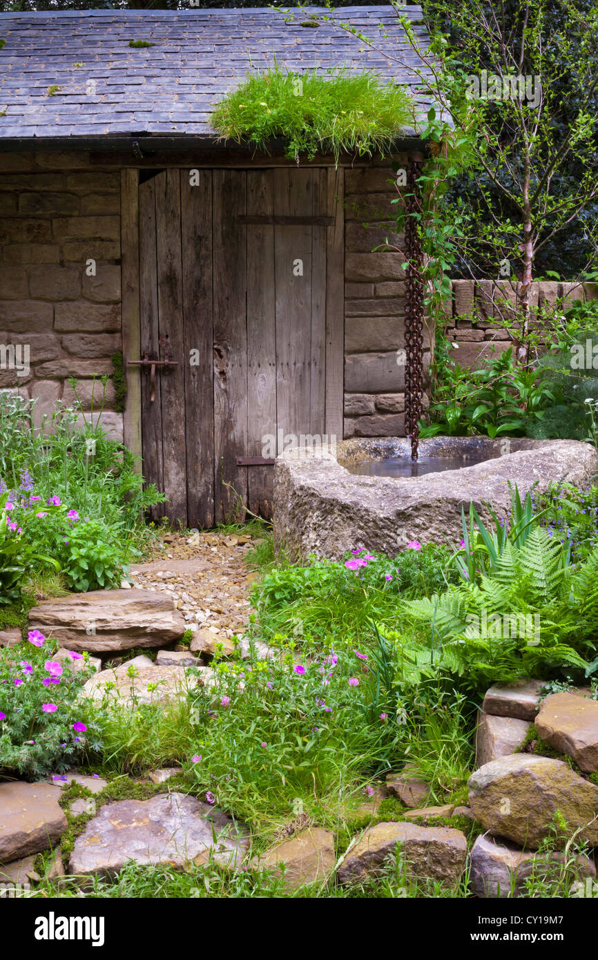 Rustic stone crofter's hut with water-chain drain leading into old well. Stock Photo
