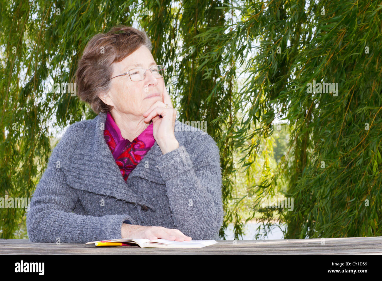 Senior woman reading outdoors, looking away. Stock Photo