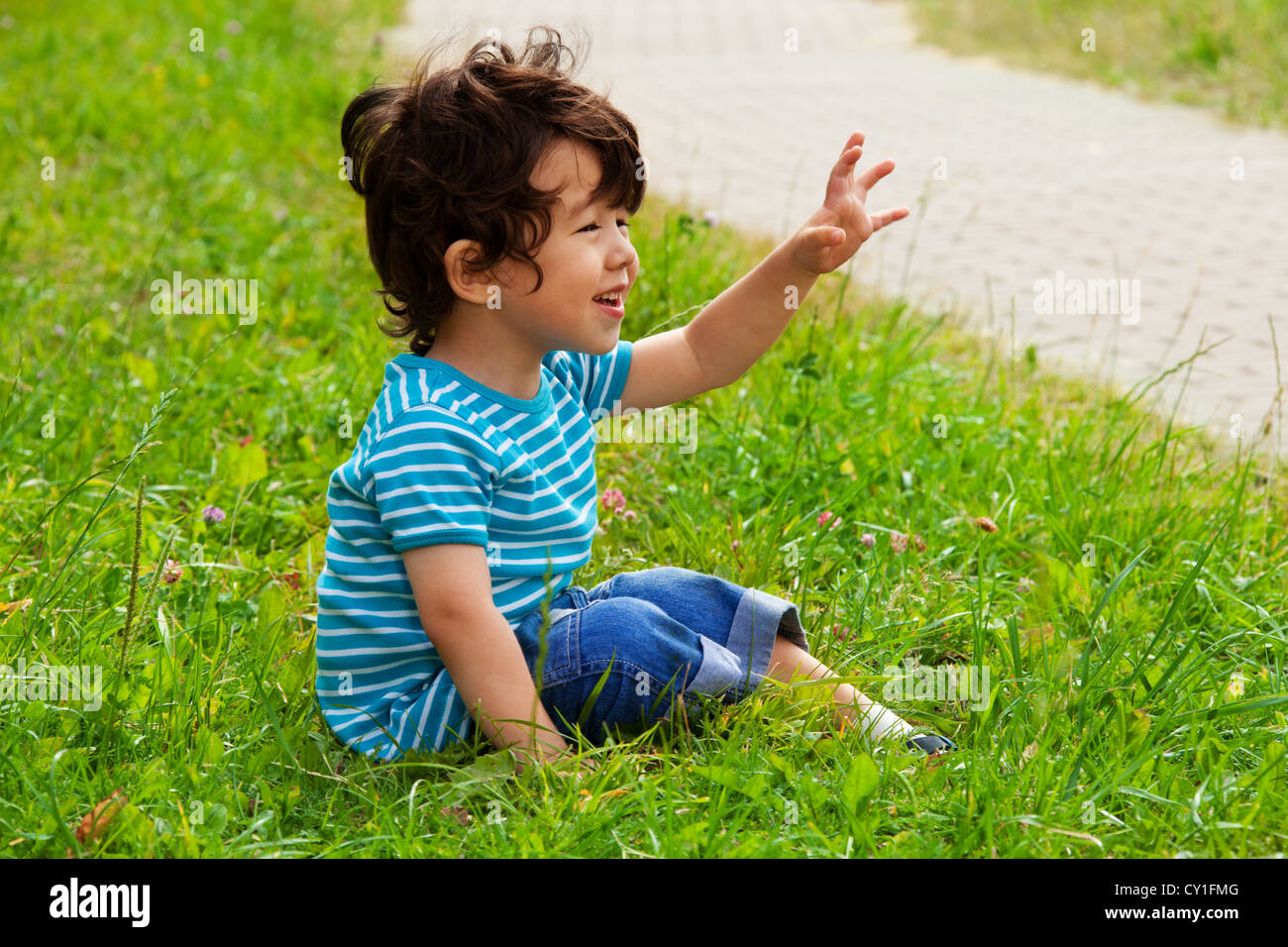 little boy sitting and waving in the park Stock Photo