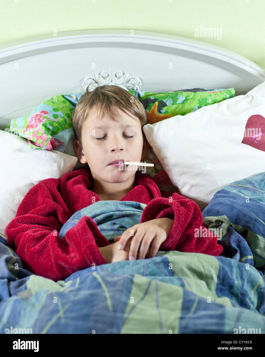 Young caucasian boy in bed with a thermometer in his mouth to check if