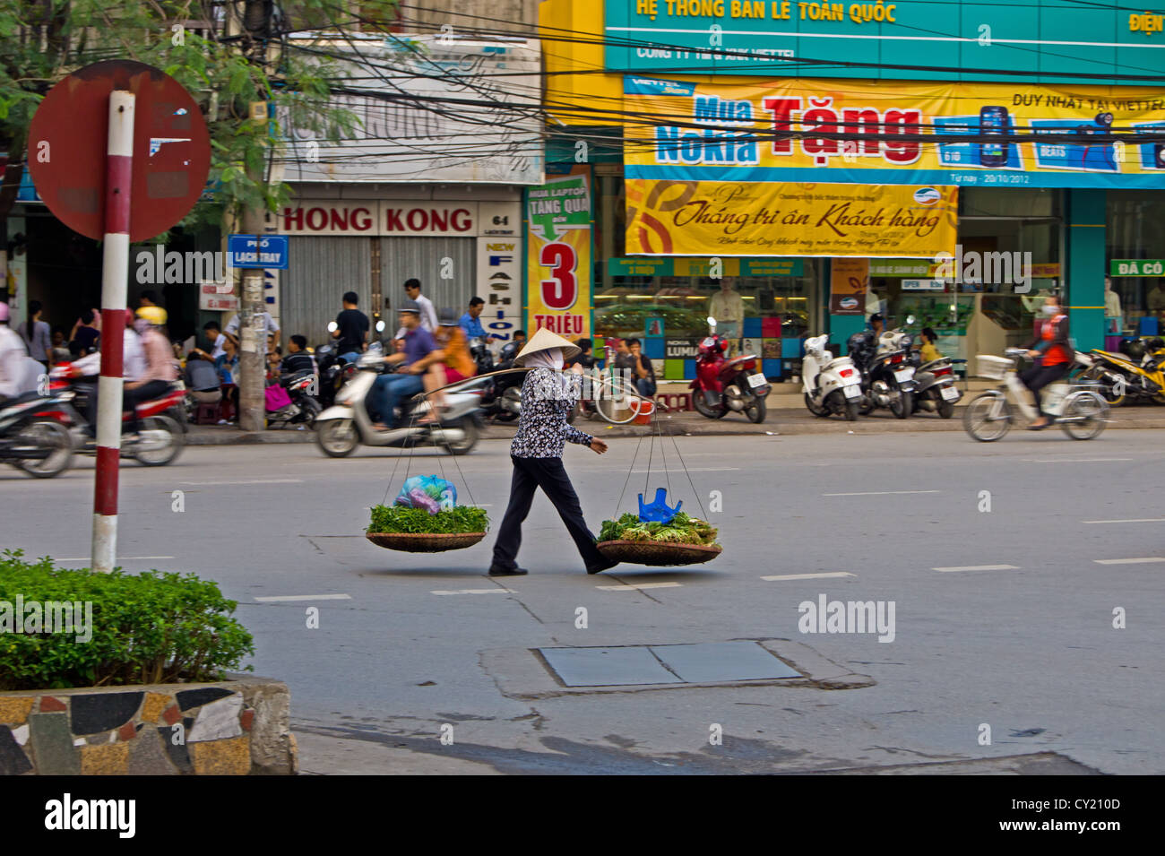A Vietnamese lady walking along a busy street road with her baskets of vegetables for sale in Hai Phong Vietnam Stock Photo