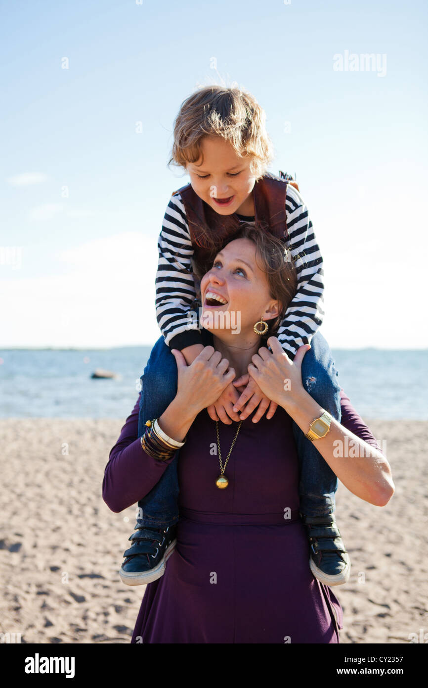 Mother carrying son on shoulders and having fun together at the beach ...