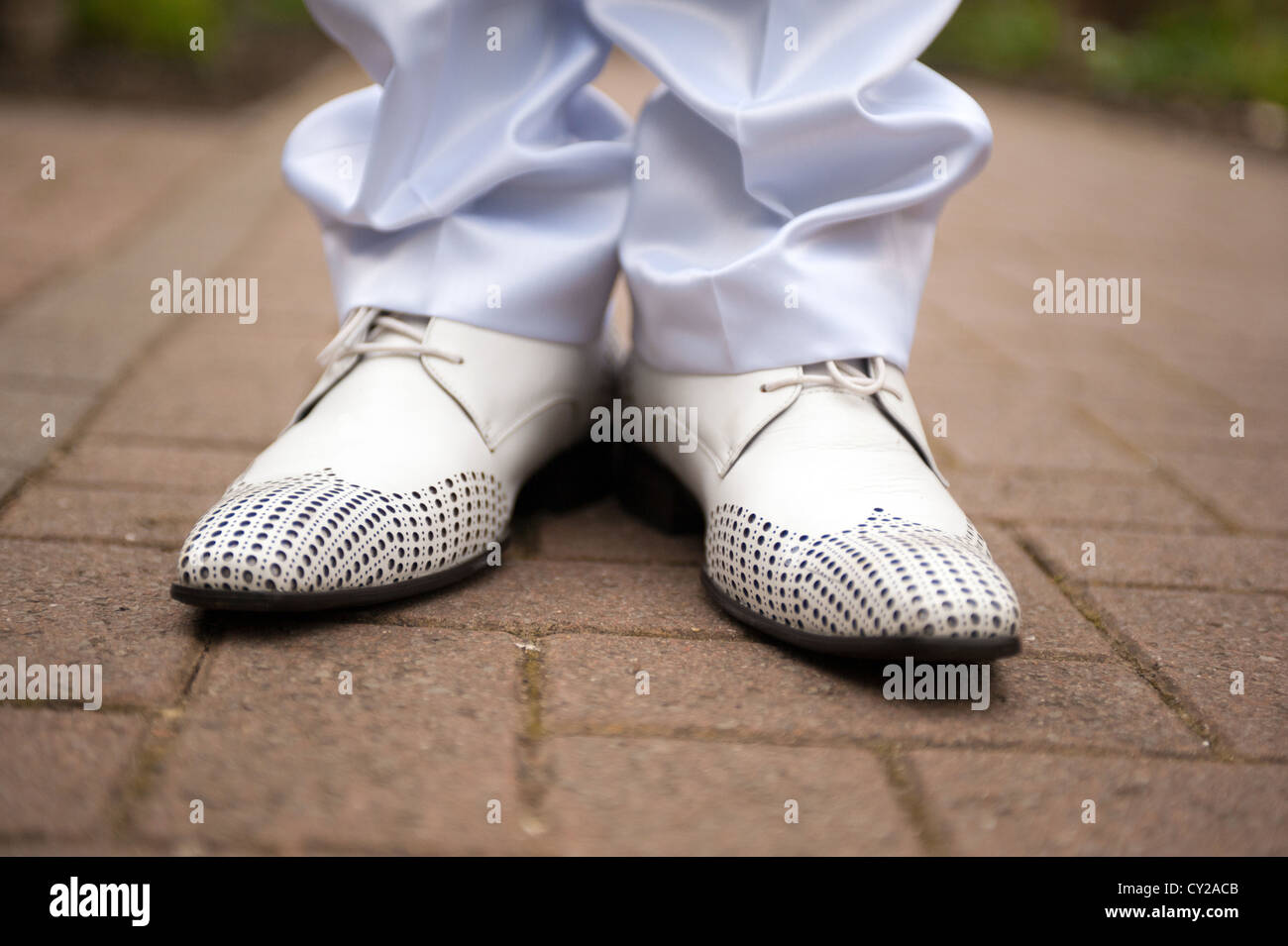 A closeup of a bridegrooms feet in white shoes stood on a pavement Stock Photo