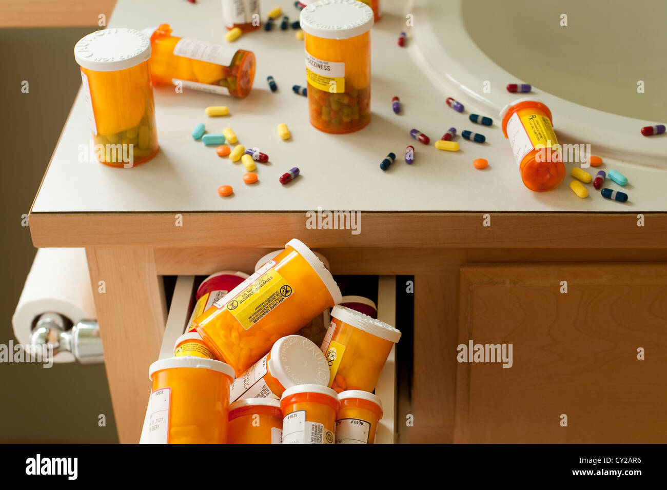 Pills and pill bottles scattered over sink counter in bathroom with drawer stuffed with pill bottles Stock Photo