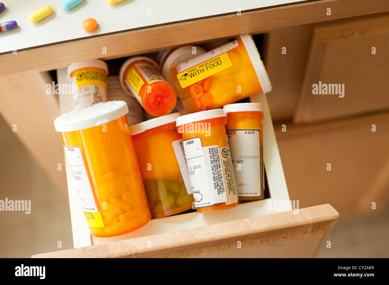 Pills and pill bottles scattered over sink counter in bathroom with drawer stuffed with pill bottles Stock Photo