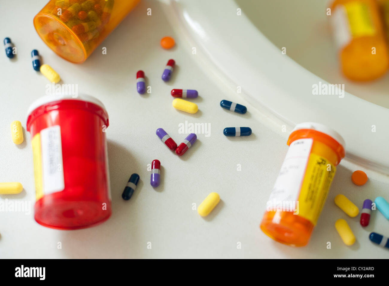 Pills and pill bottles scattered over sink counter in bathroom Stock Photo