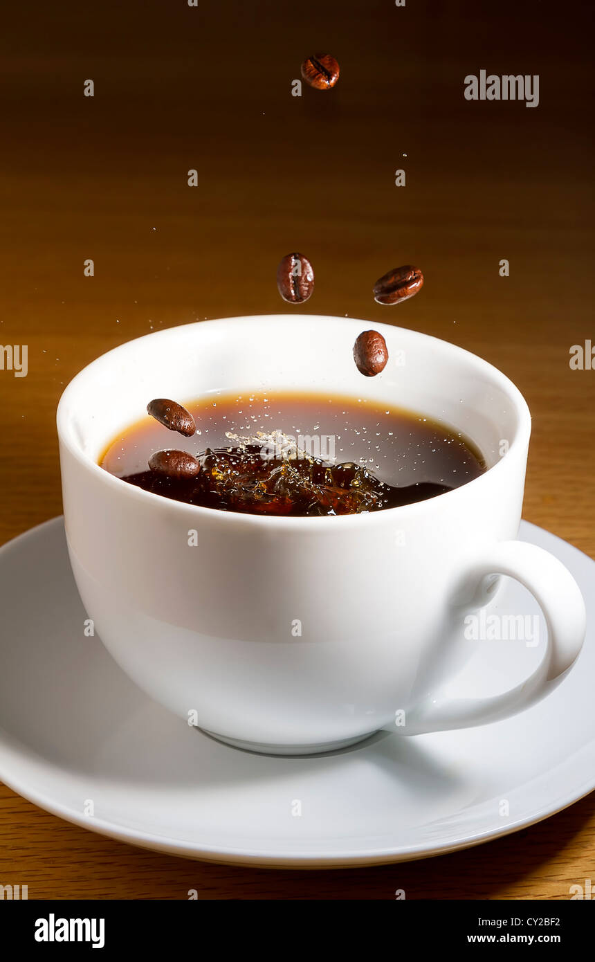 Cup of black coffee with beans dropping in Stock Photo - Alamy