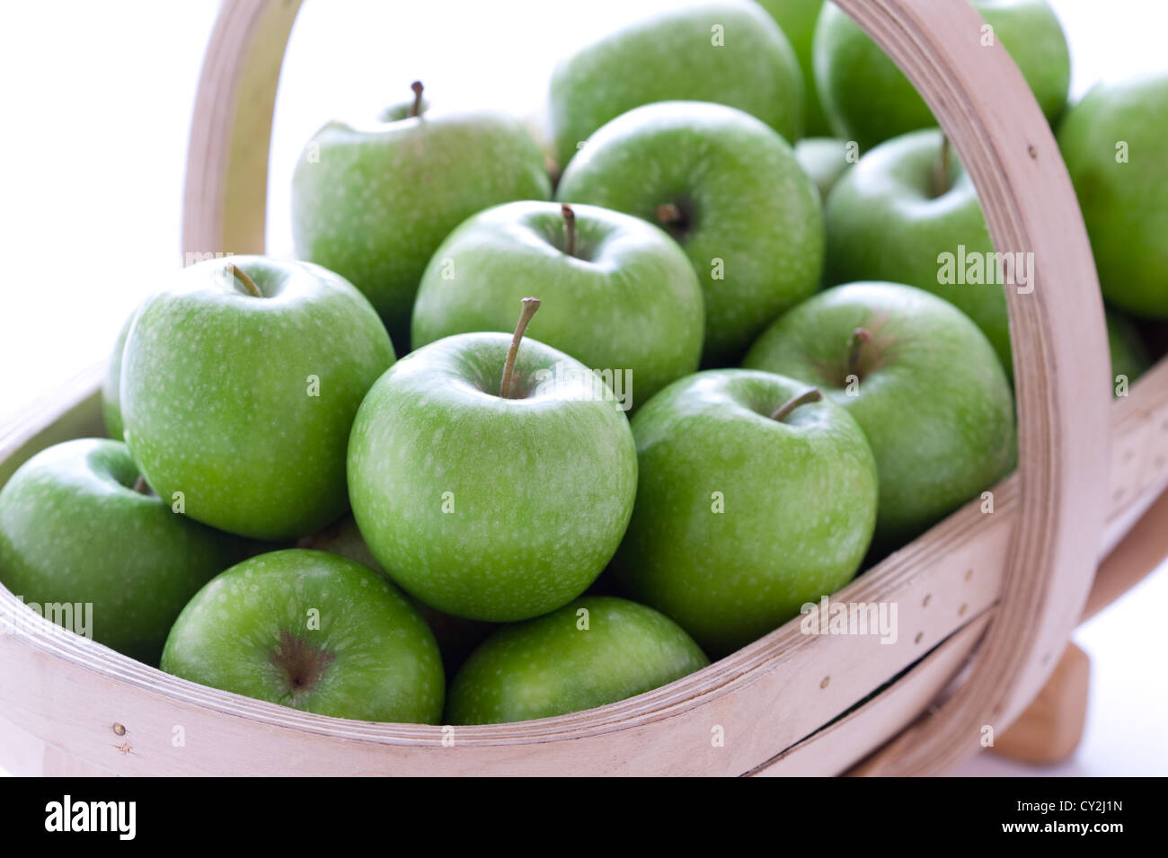 fresh harvested green granny smith apples in a wooden trug on a white background studio macro shot Stock Photo
