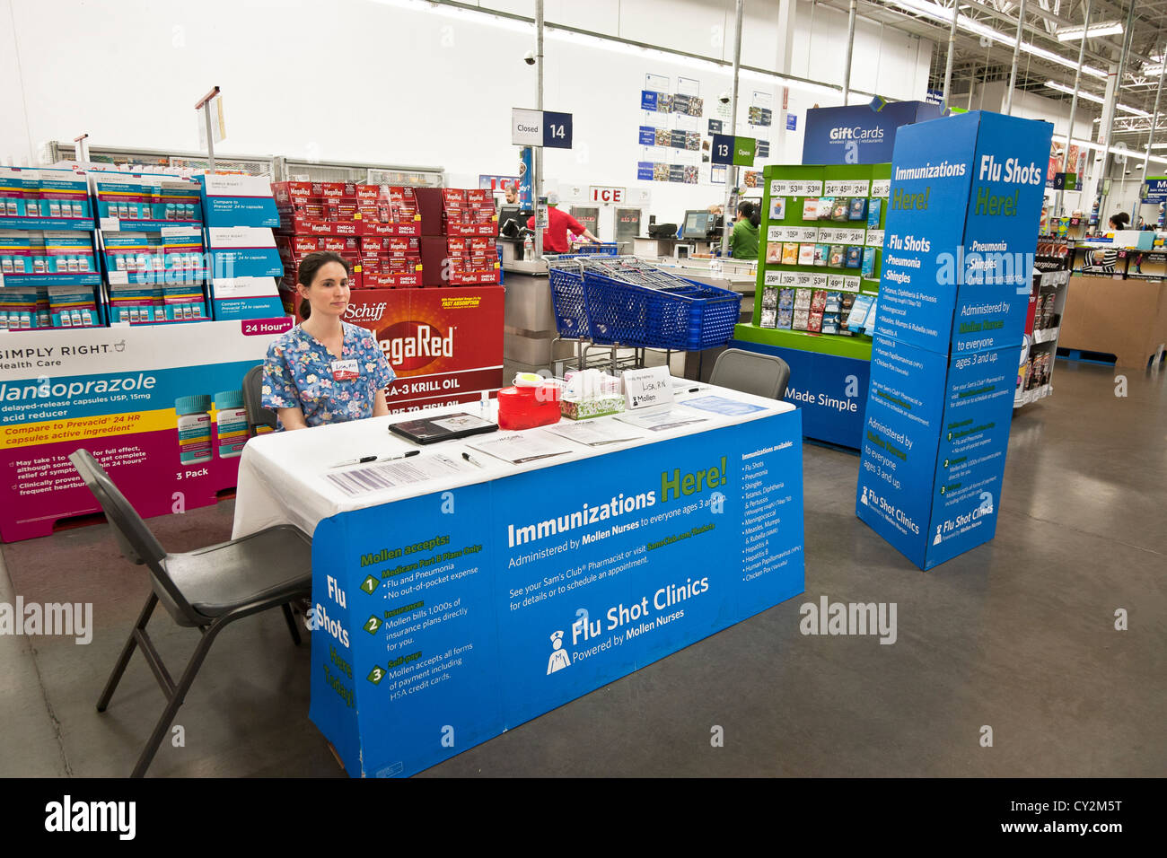 pretty young nurse sits at table offering flu shots next to check out counters in Sams Club membership only retail warehouse Stock Photo
