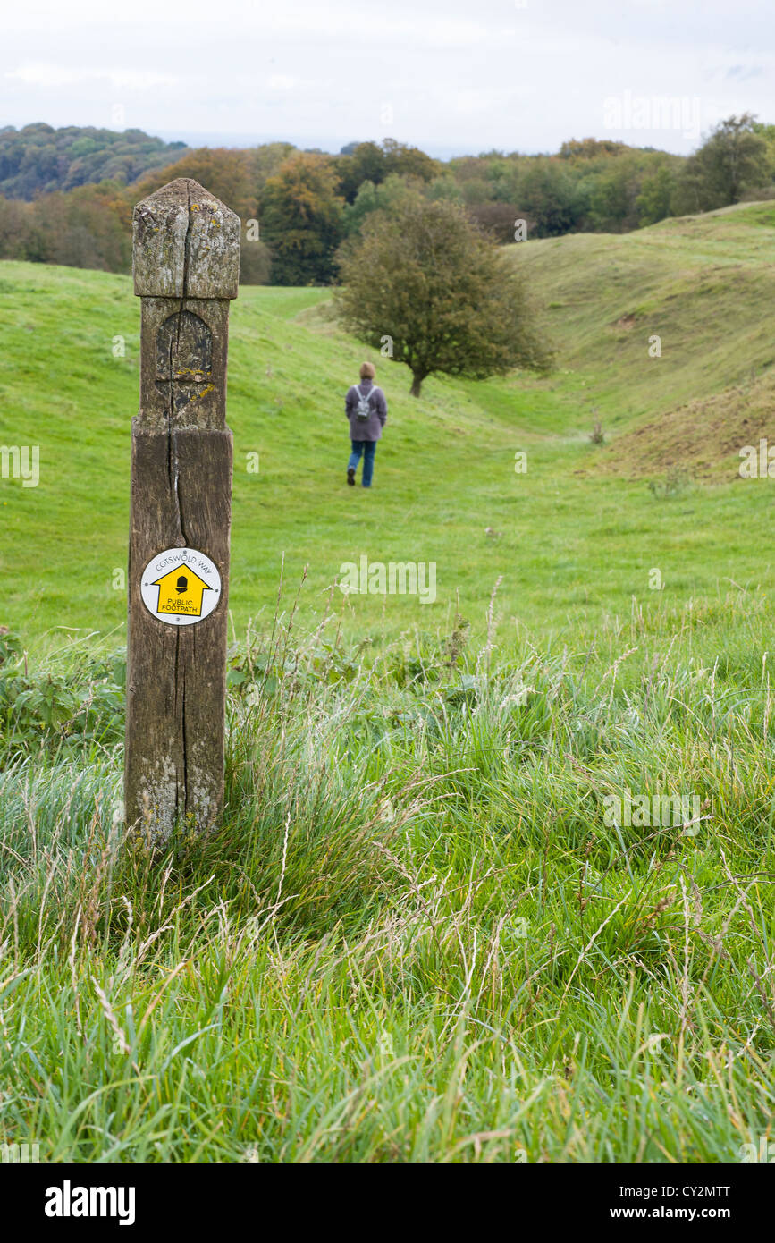 View of the Cotswold way footpath, with signpost and female walker in distance, Worcestershire, England Stock Photo