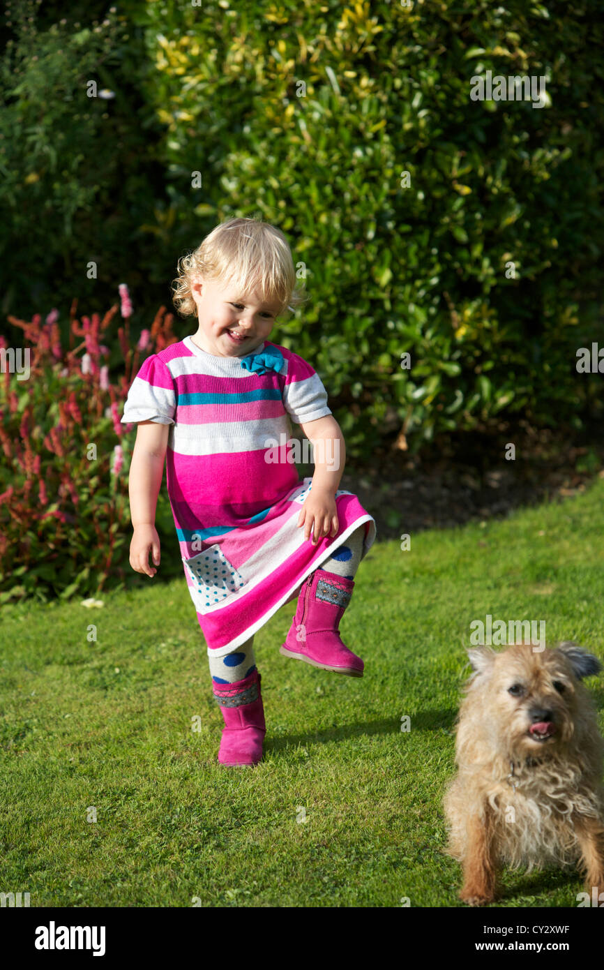 Small blonde girl in pink dress dances with a dog in a garden Stock Photo