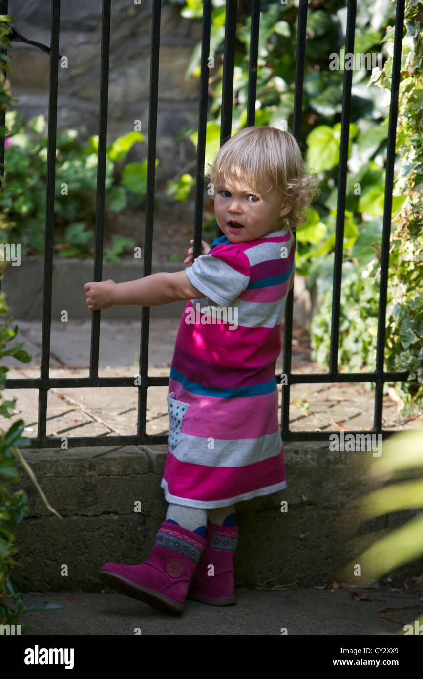 Little girl in a striped dress standing at a garden gate Stock Photo