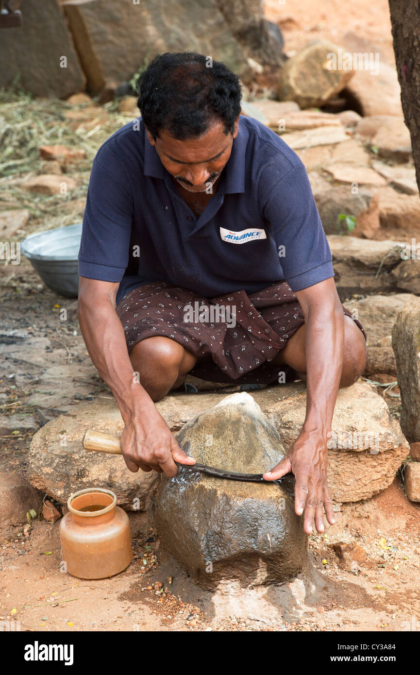 Indian village man sharpening a harvesting sickle on a stone in a rural indian village. Andhra Pradesh, India Stock Photo