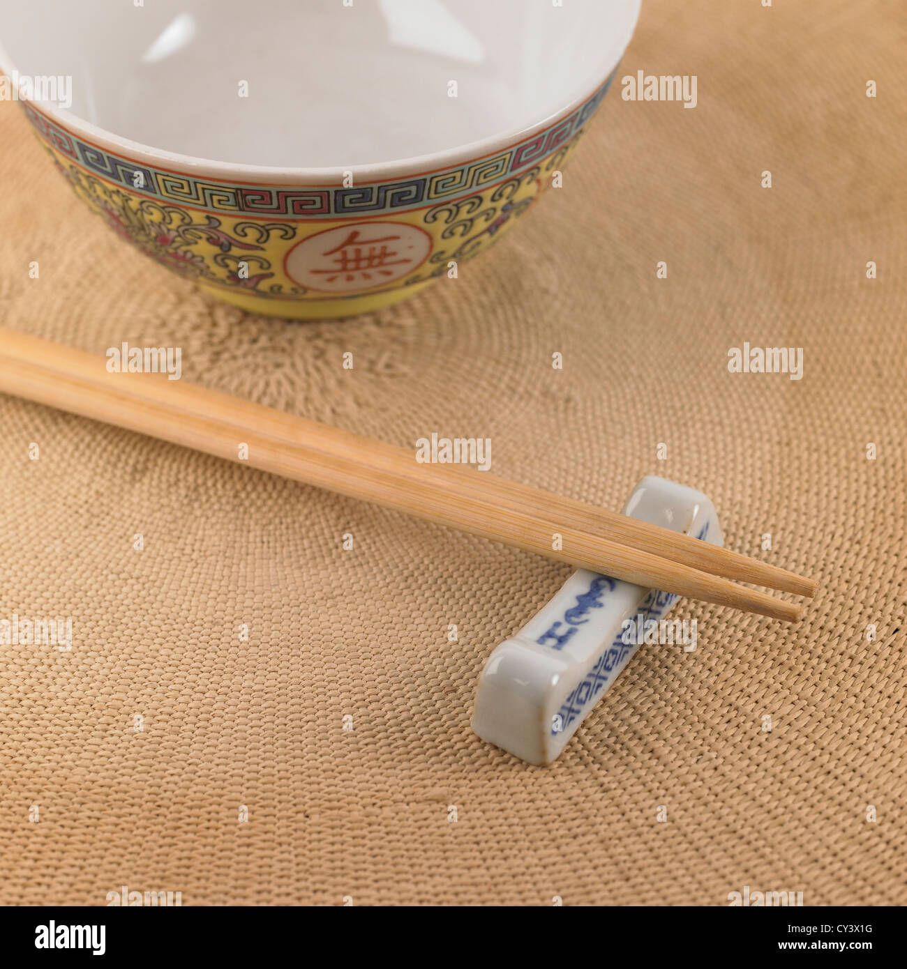 Wooden chopsticks resting on a glazed chopstick holder and mat with bowl in background Stock