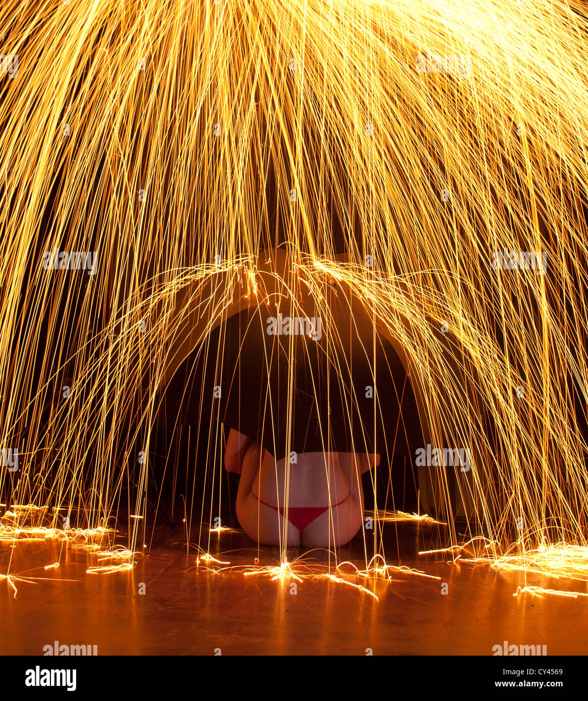 Woman with umbrella sits under a downpour of sparks Stock Photo