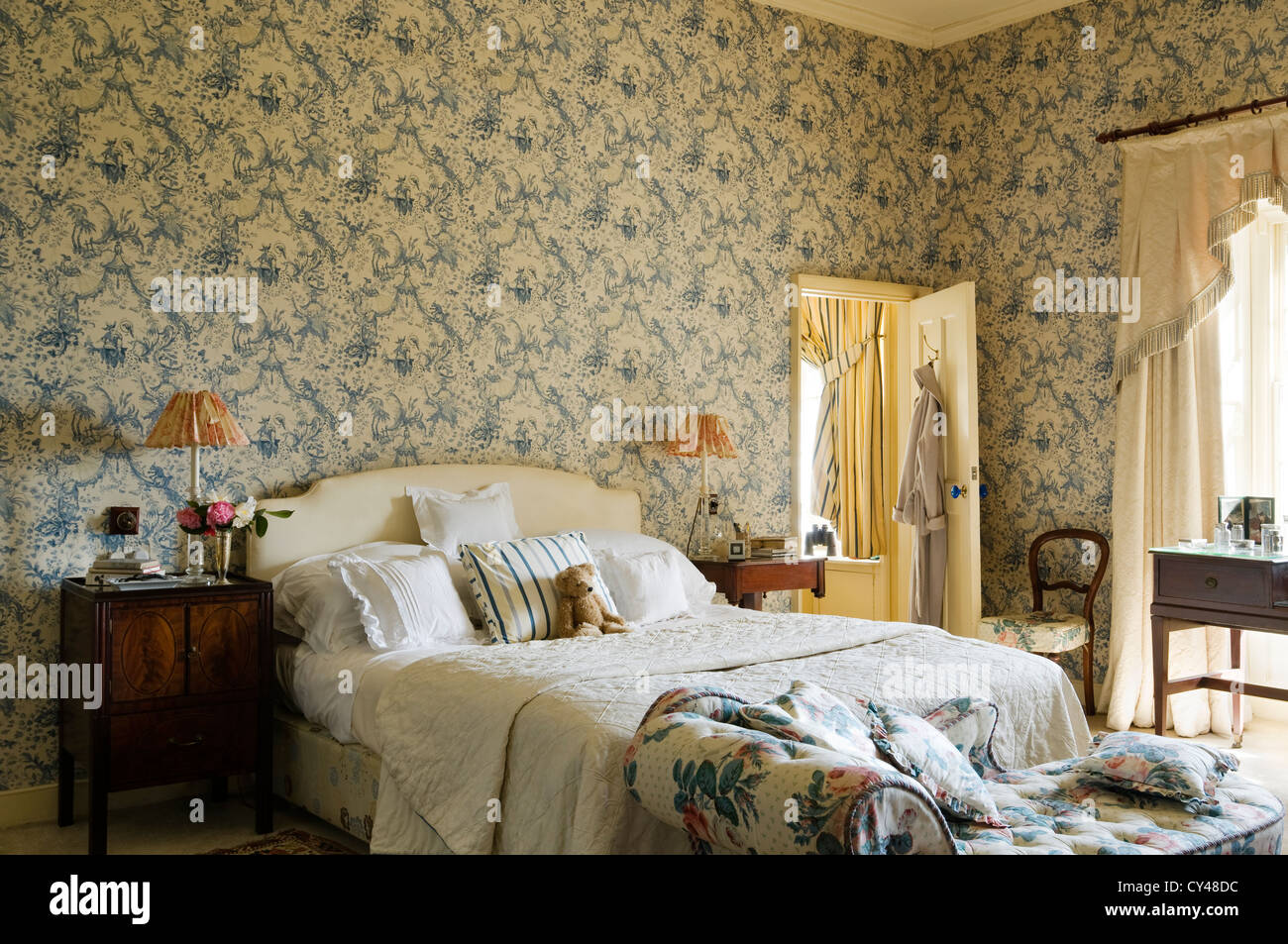 Toile de jouy wallpaper in bedroom with floral patterned chaise lounge at the foot of the bed Stock Photo
