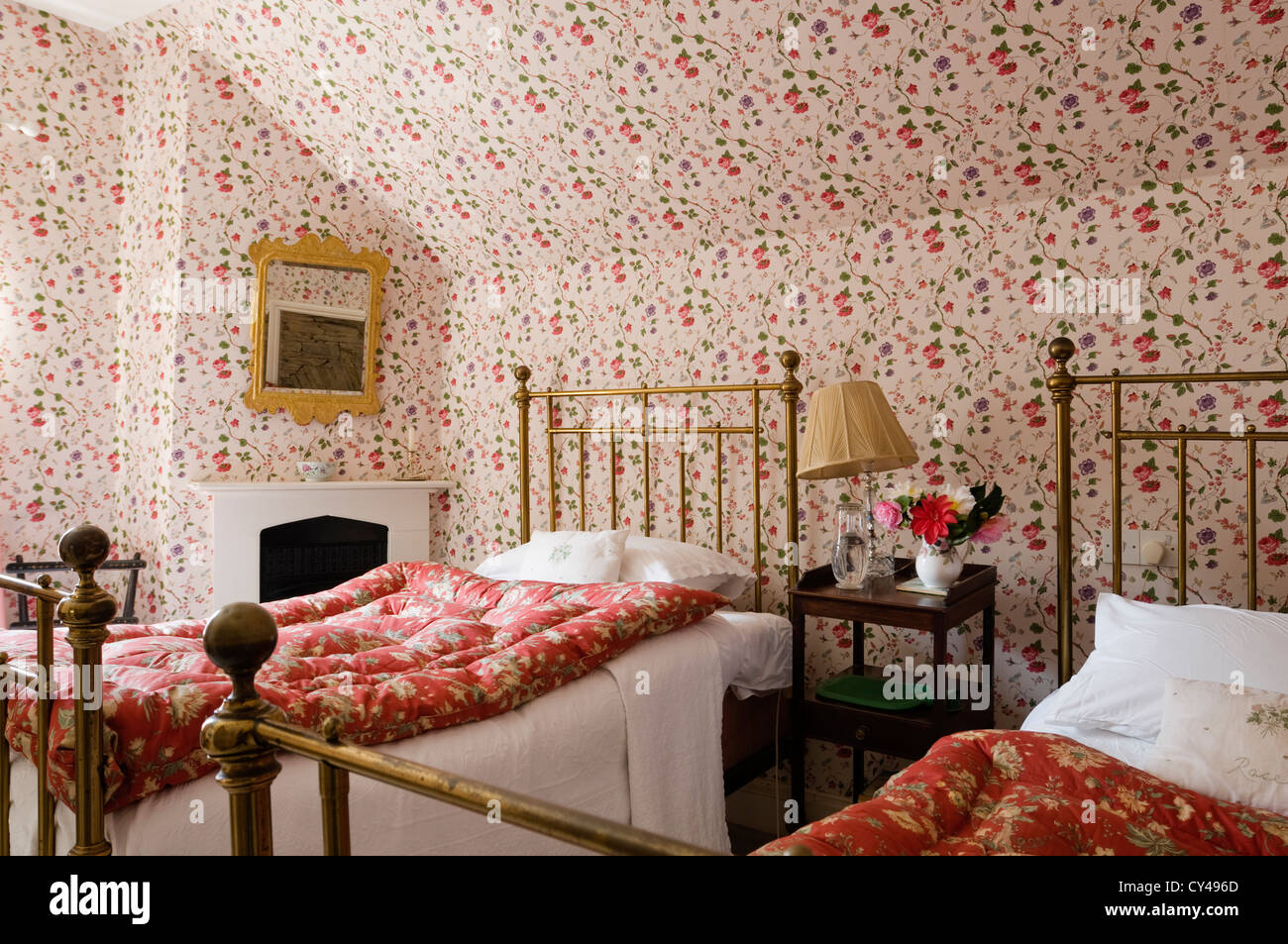 Twin wrought iron beds in bedroom with floral patterned wallpaper and red floral eiderdowns Stock Photo