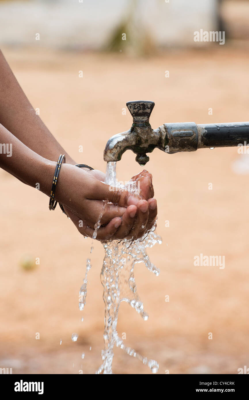 Indian girl drinking water in cupped hands at a communal water tap in