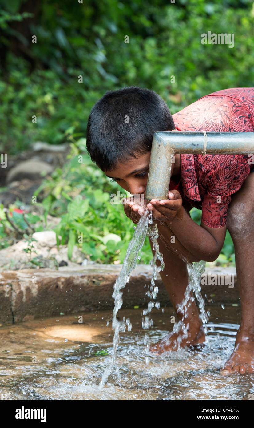 Young Indian boy drinking water from a hand water pump in rural indian village. Andhra Pradesh, India Stock Photo