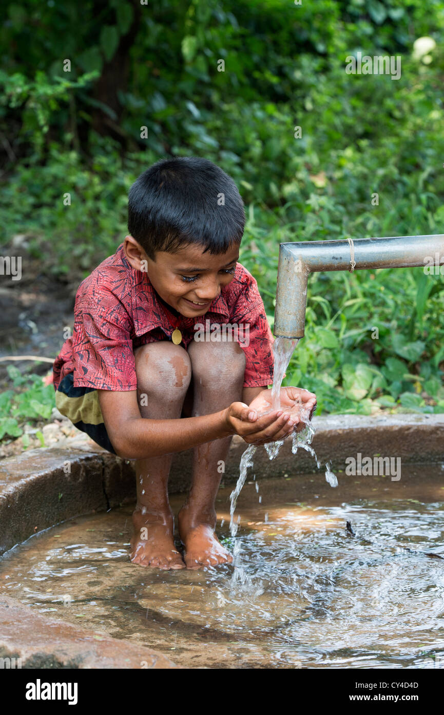 Young Indian boy drinking water from a hand water pump in rural indian village. Andhra Pradesh, India Stock Photo