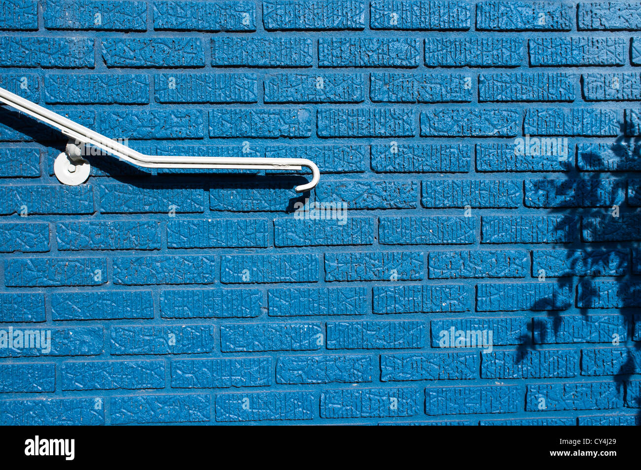 A white railing and shadows contrast against a brightly painted blue brick wall. Stock Photo