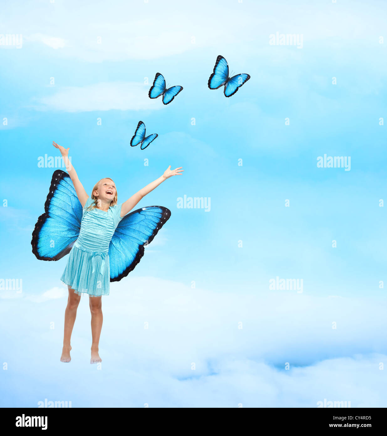Happy Young Girl in Blue Dress with Arms in the Air Releasing Butterflies Stock Photo