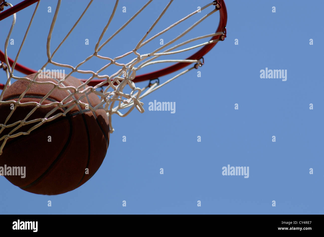 Basketball going through net against blue sky Stock Photo