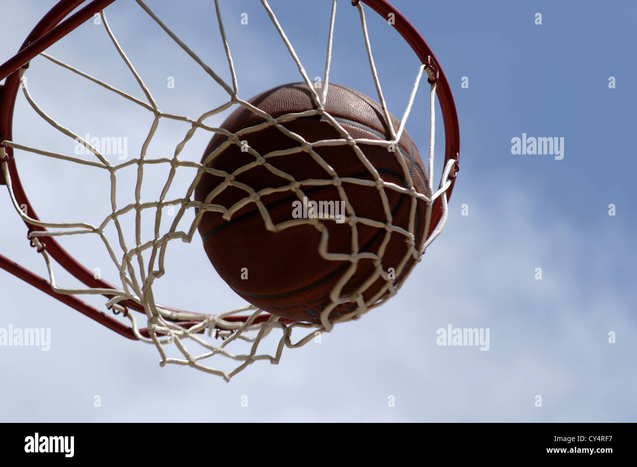 Basketball going through net with a blue cloudy sky background Stock Photo