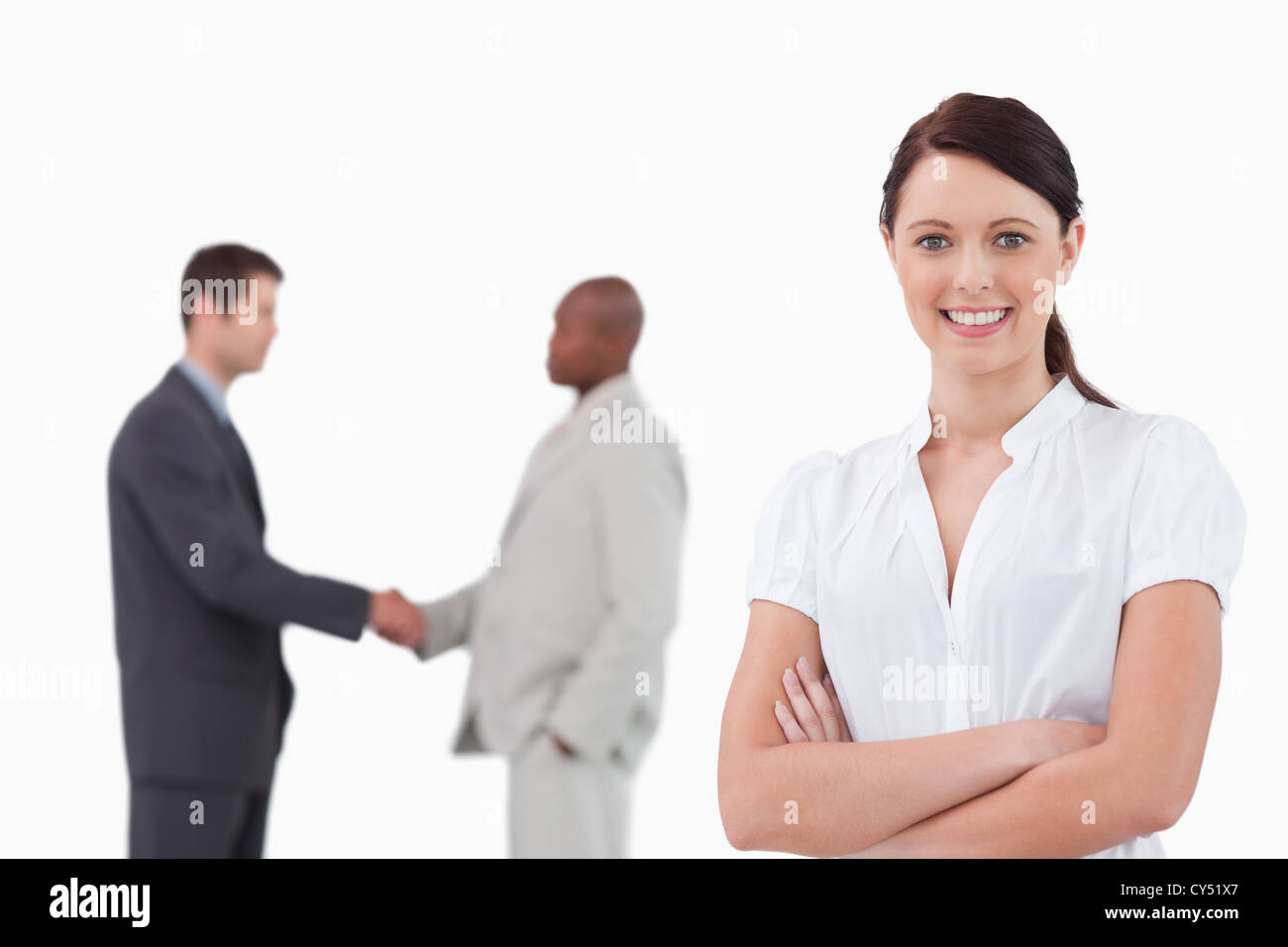Businesswoman with arms folded and hand shaking trading partners behind her Stock Photo