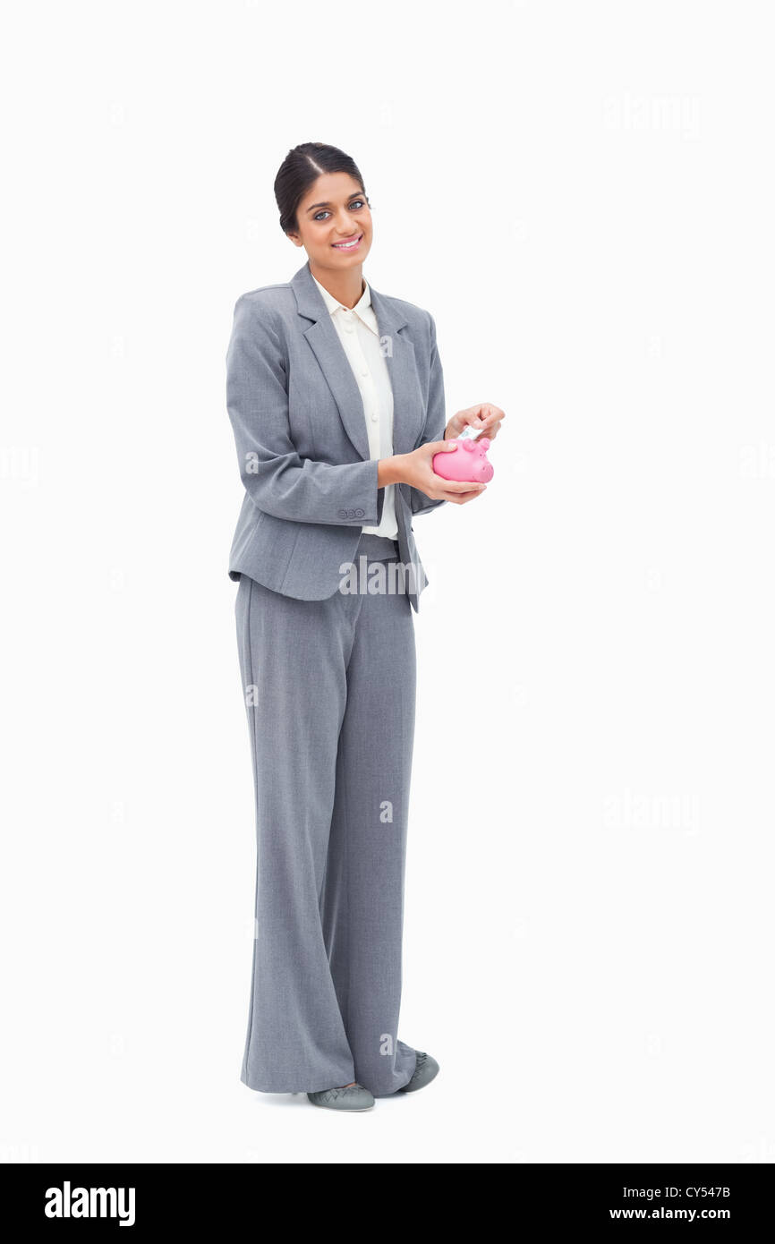 Smiling female banker putting money into piggy bank Stock Photo