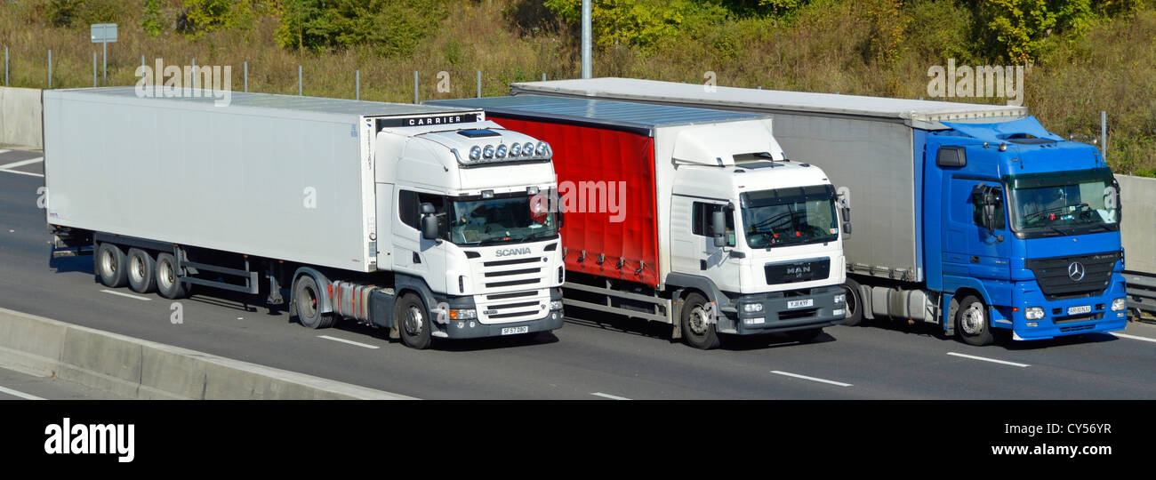 Red white & blue colours on overtaking transport supply chain lorry truck vehicles driving along four lane M25 motorway road Essex England UK Stock Photo