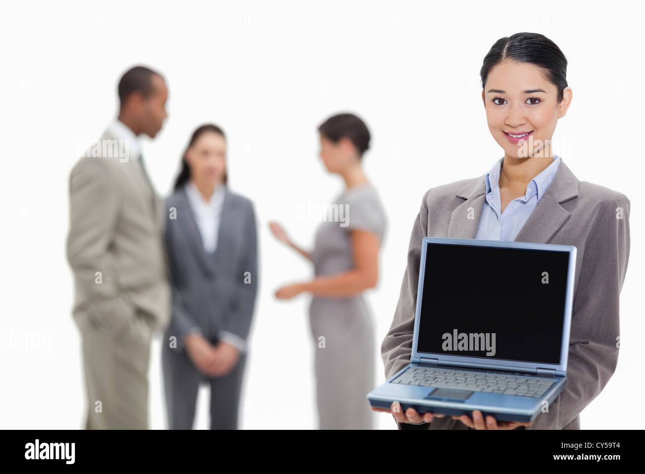 Businesswoman smiling showing a laptop screen with co-workers in the background Stock Photo