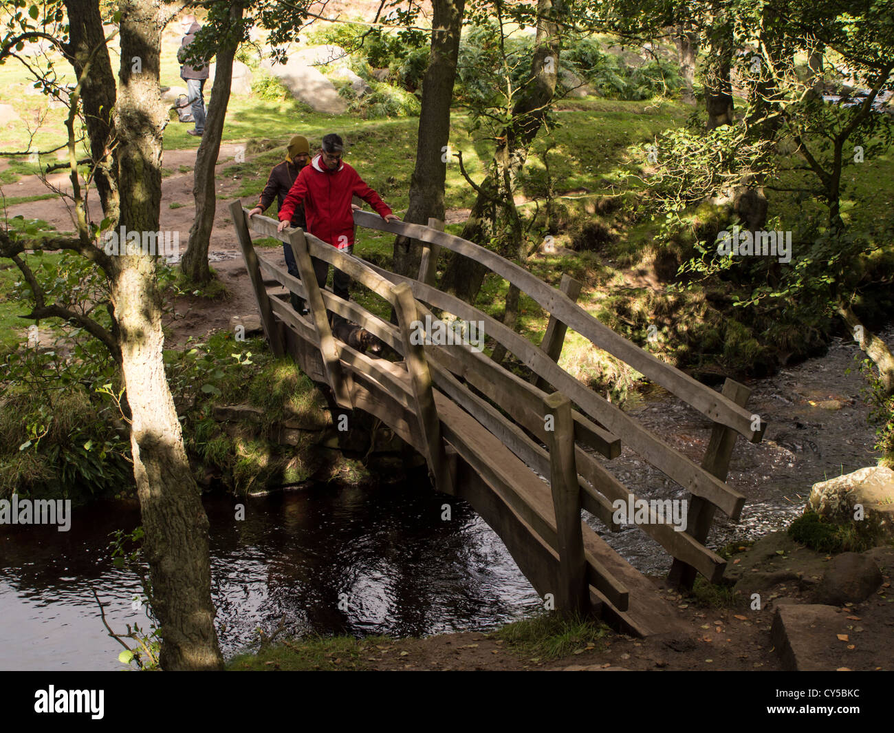 people crossing a small wooden footbridge in the peak district stock