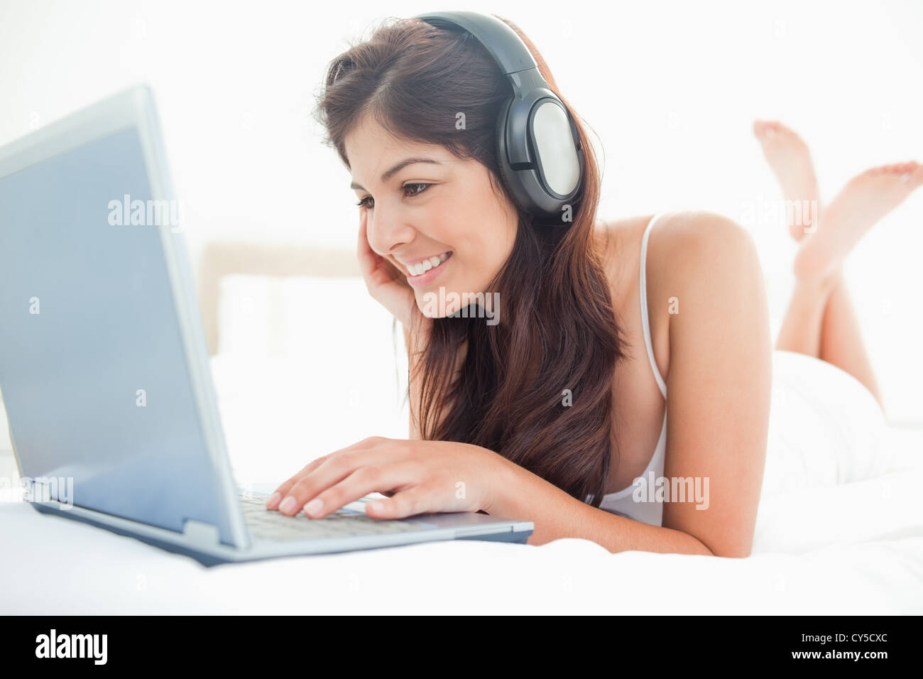 Woman watching her laptop screen and listening to her headphones with crossed legs resting on a bed Stock Photo