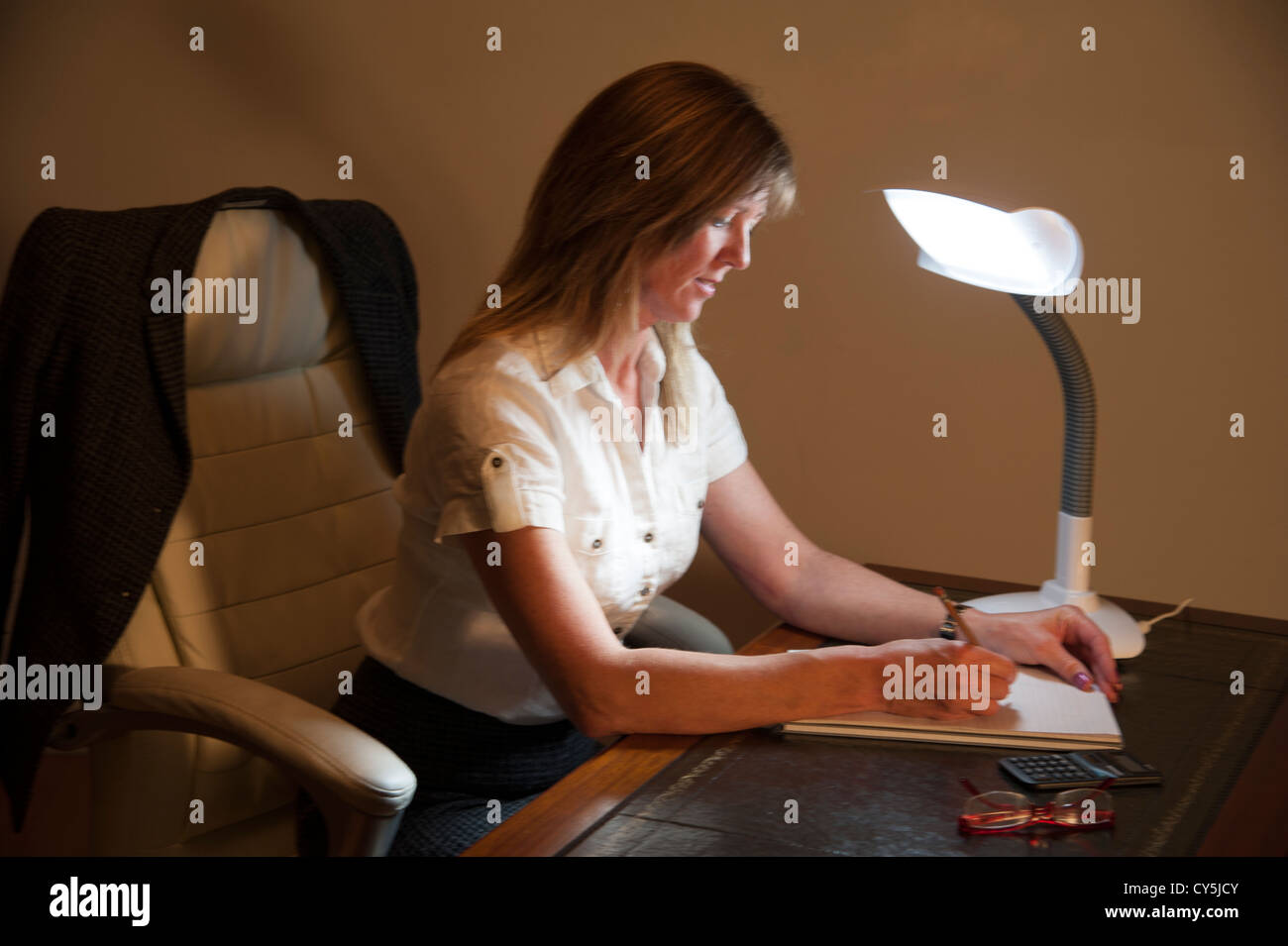 Woman and SAD table lamp. Seasonal Affective Disorder sufferer sitting at a desk Stock Photo