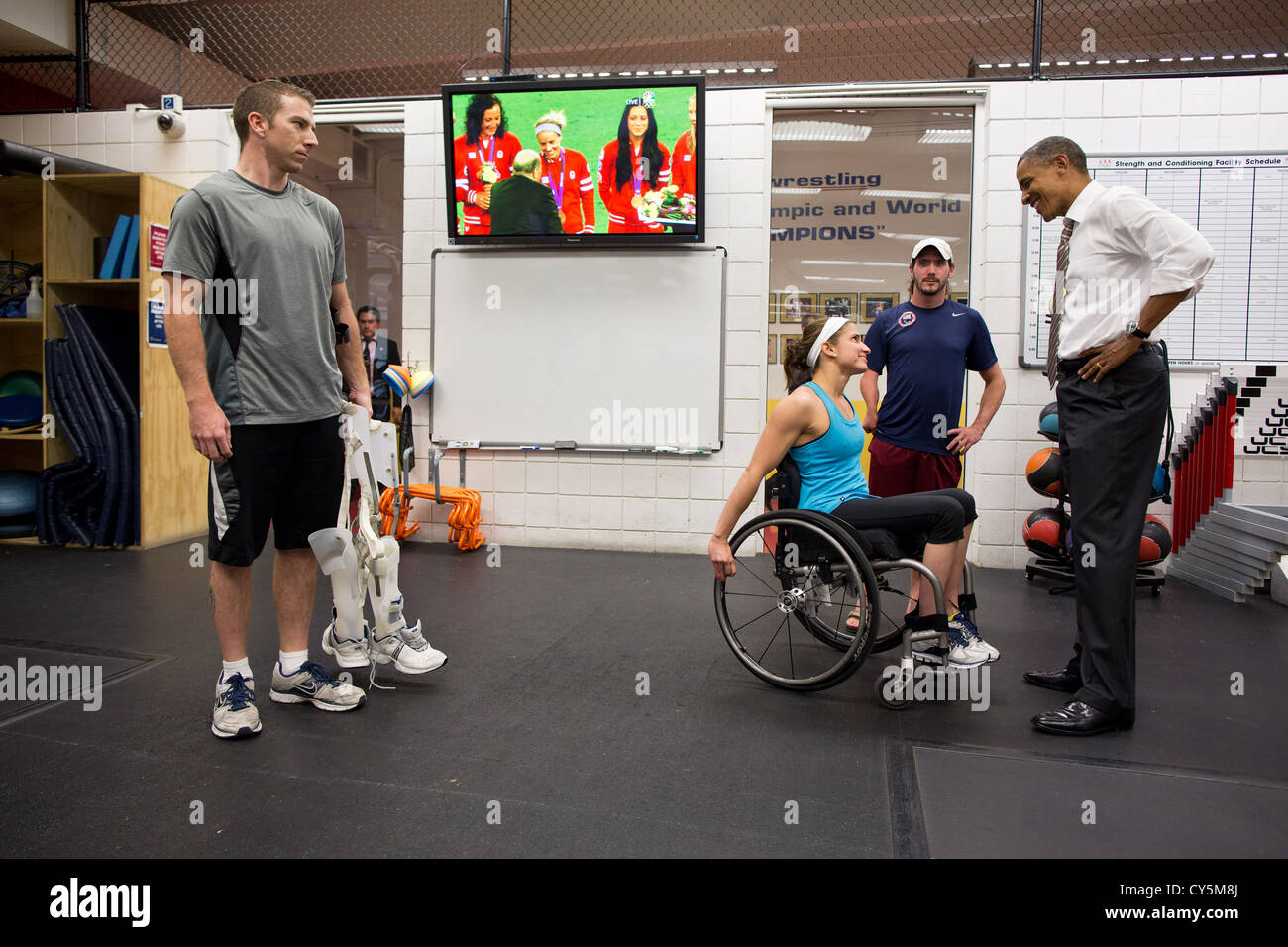 US President Barack Obama talks with paralympic athletes at the US Olympic Training Facility August 9, 2012 in Colorado Springs, Colorado. Broadcast of the gold medal ceremony for the US Olympic women's soccer team plays on the TV in the background. Stock Photo