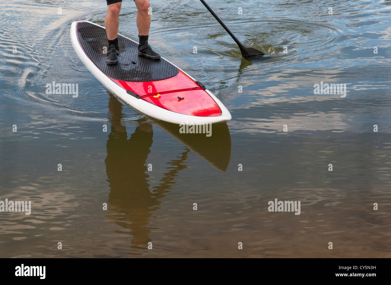 paddling stand up paddleboard on a lake - feet and legs of male paddler Stock Photo