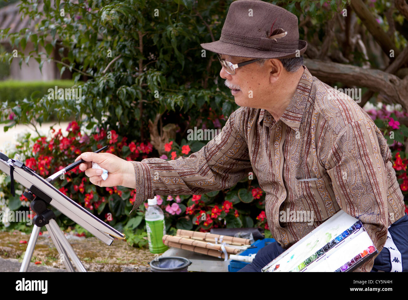 An elderly Okinawan man painting in the grounds of Ryukyu Mura - a theme park dedicated to celebrating ancient Okinawan culture. Stock Photo