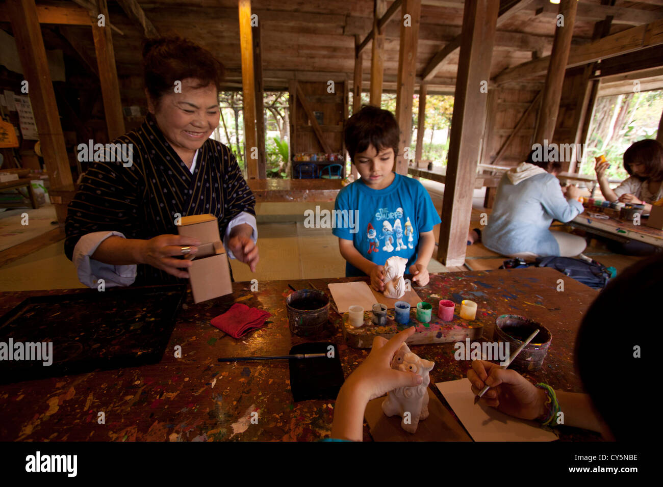 A worker at the Ryukyu Village on the main island of Okinawa, Japan helps two young boys paint pottery Shiisa - lion god statues Stock Photo