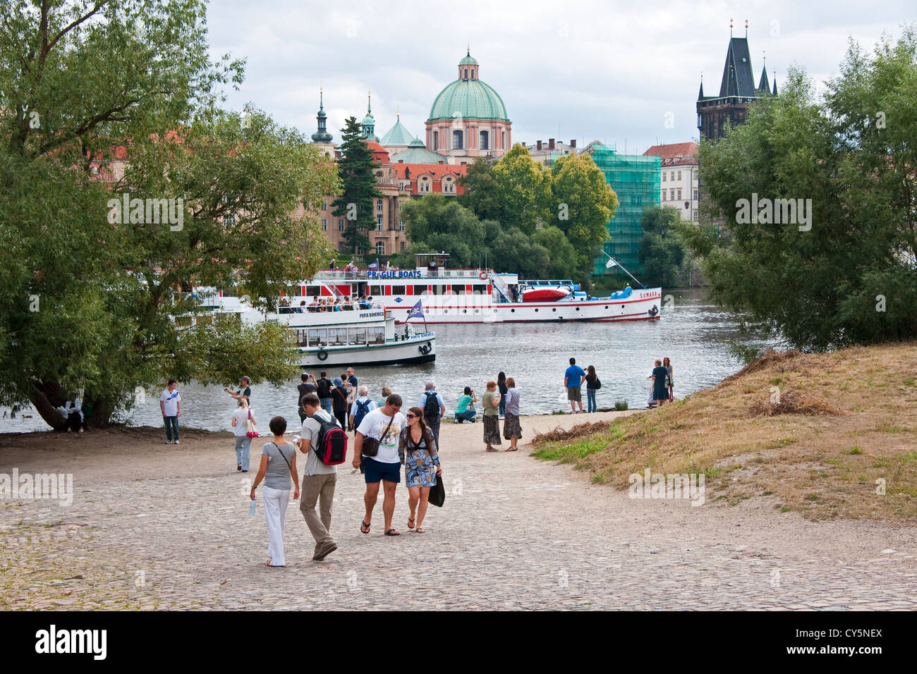 Prague tourists along Vltava River with St Francis of Assisi Church dome in background Stock Photo