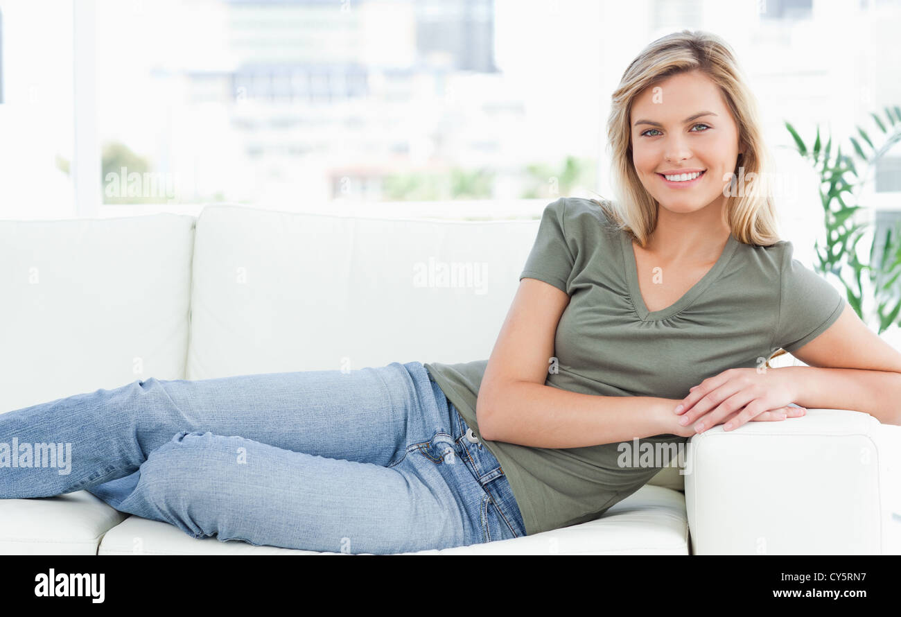 Woman lying across the couch, looking forward, smiling with arms and legs folded Stock Photo