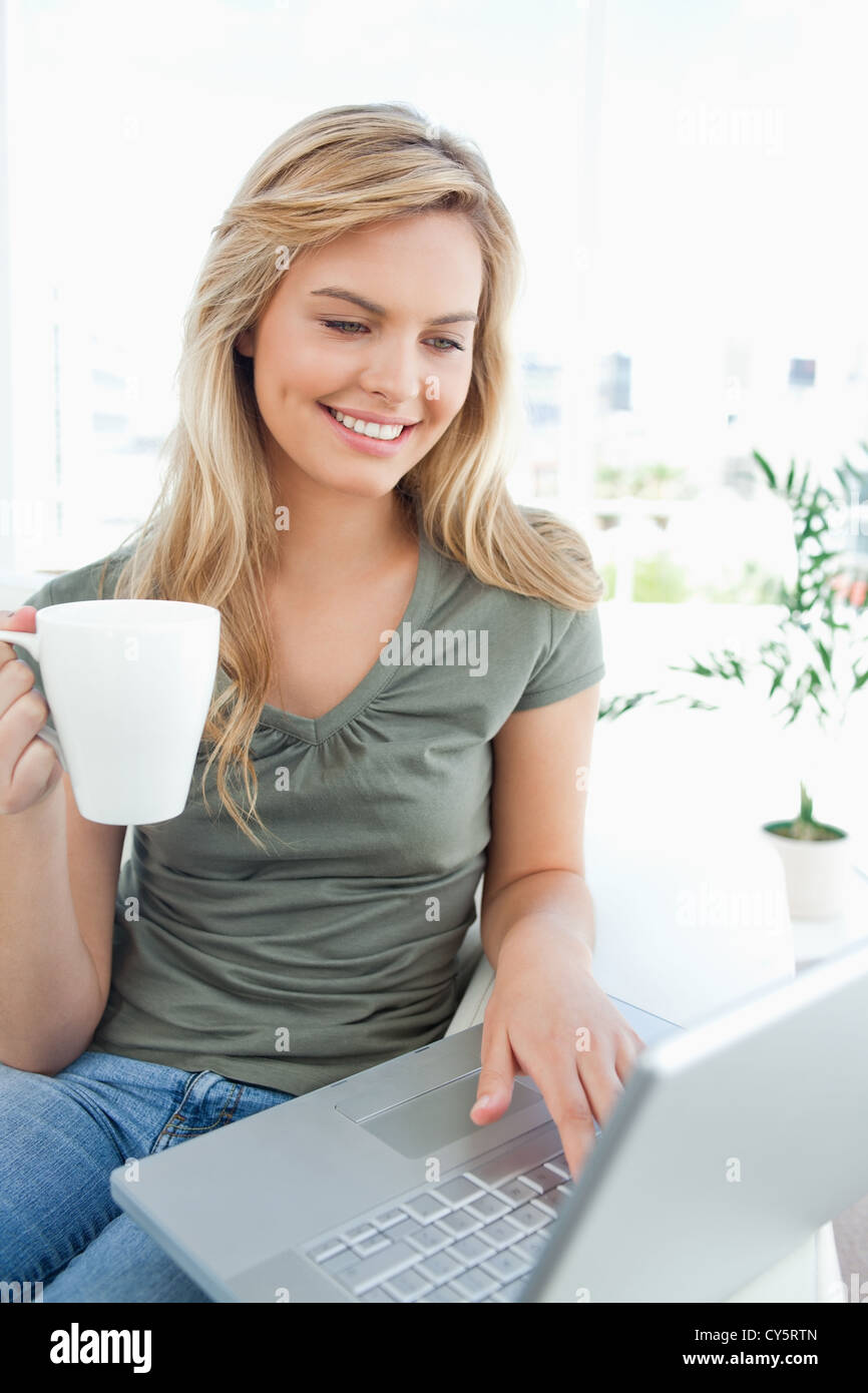 Woman smiling as she uses her laptop and holds a cup in her free hand Stock Photo