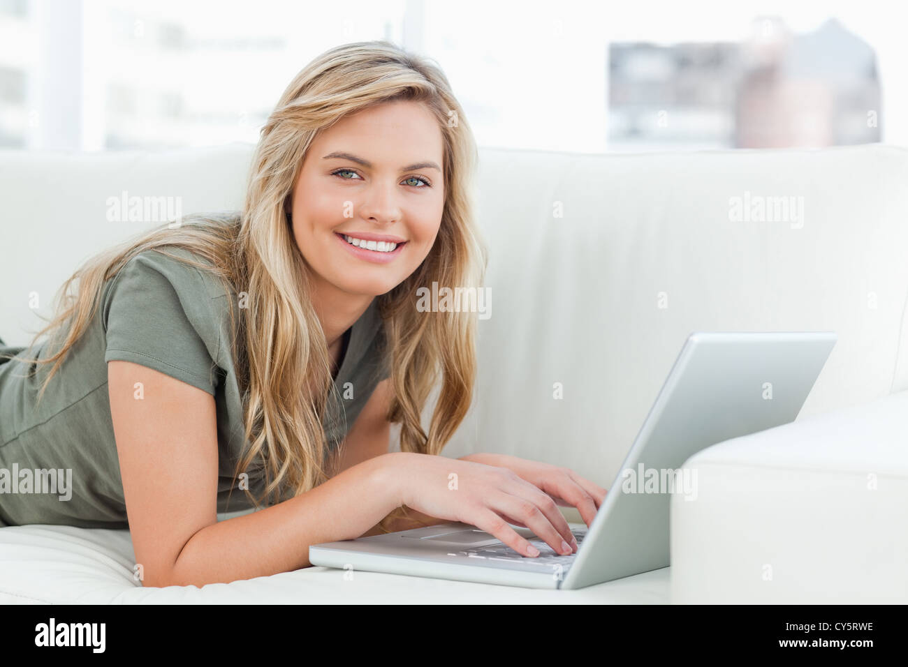 Woman lying across the couch with laptop in front of her, smiling Stock ...