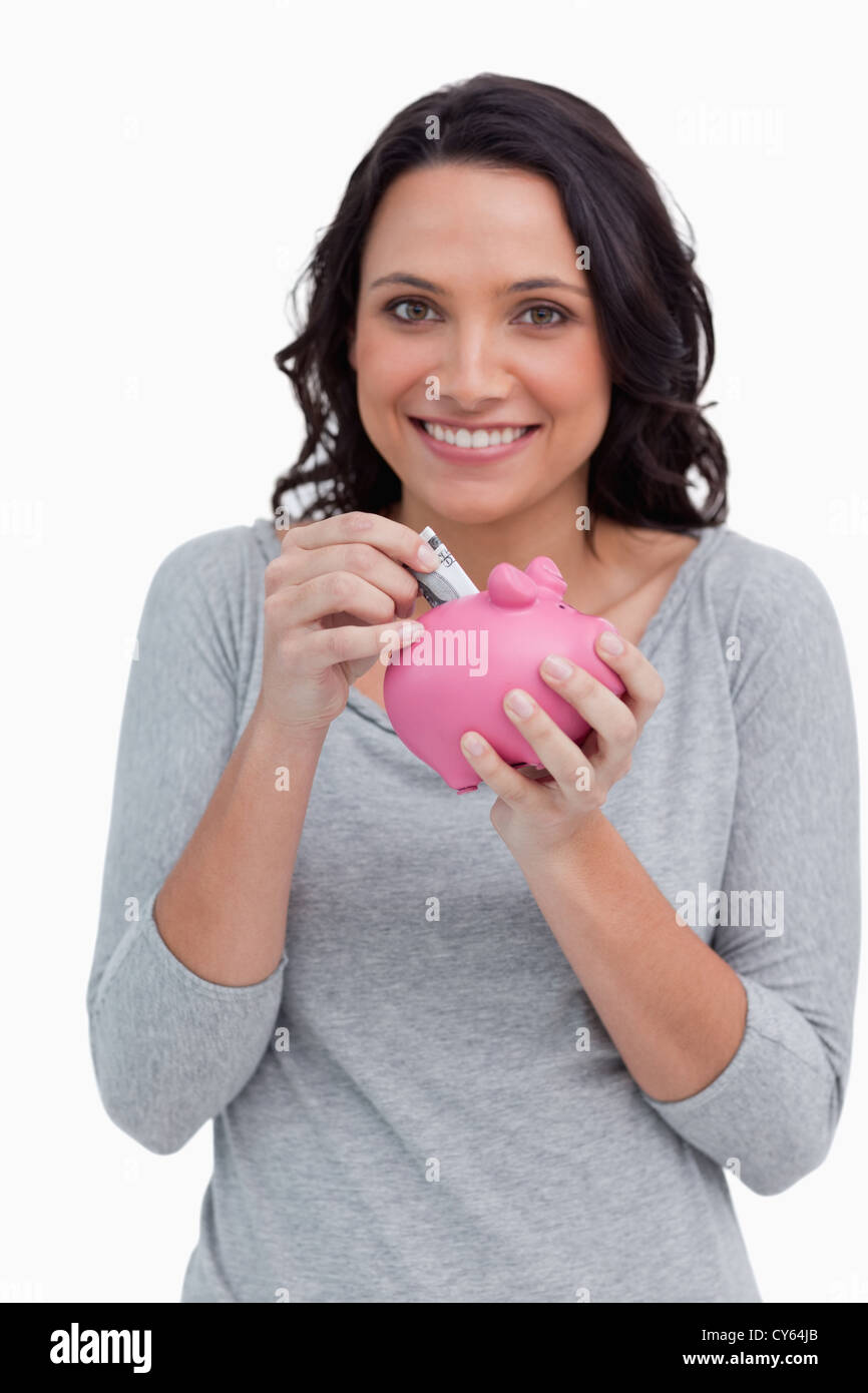 Smiling woman putting money into her piggy bank Stock Photo - Alamy