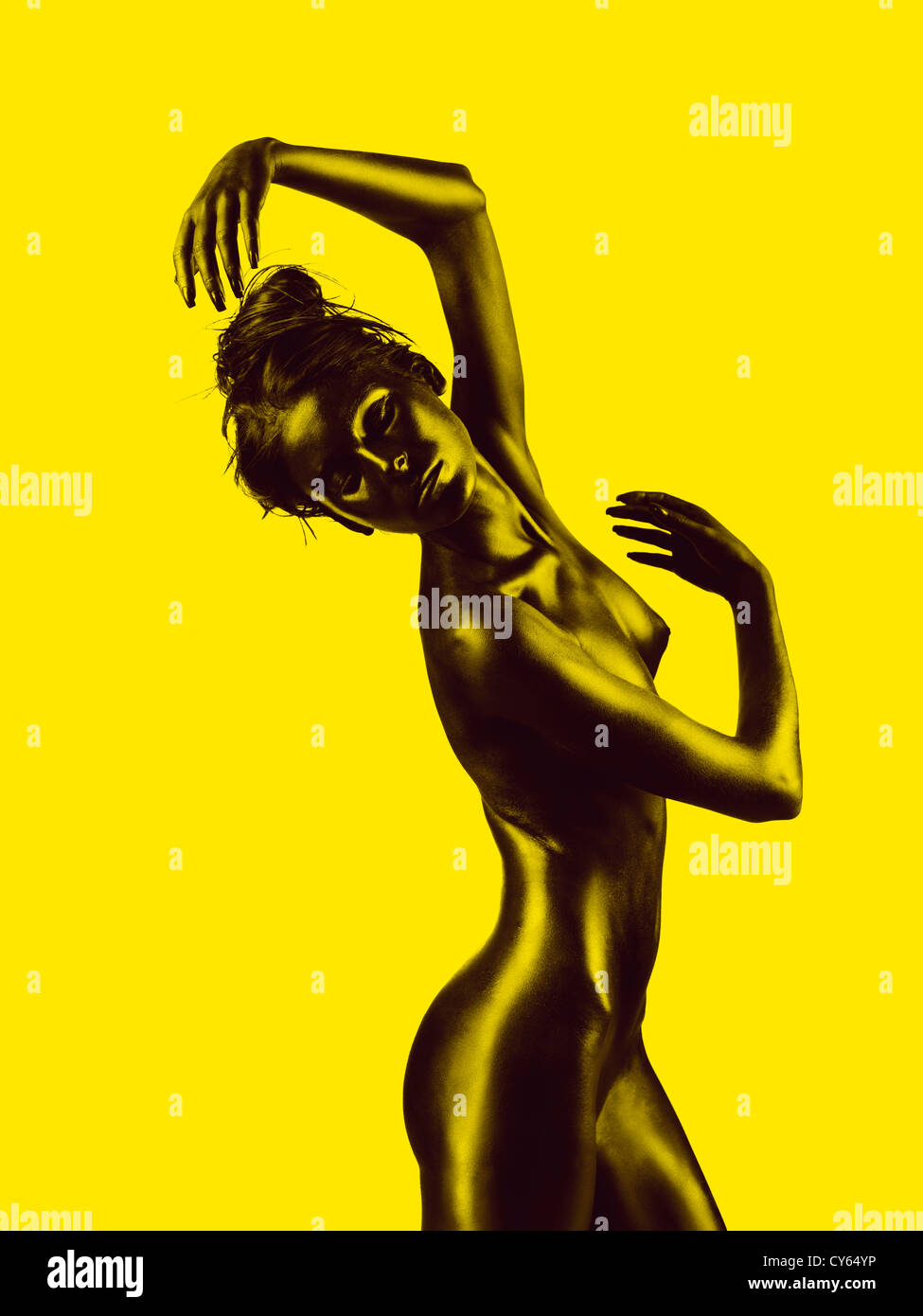 artistic nude of a young woman with black painted skin and yellow background, in a dance movement Stock Photo