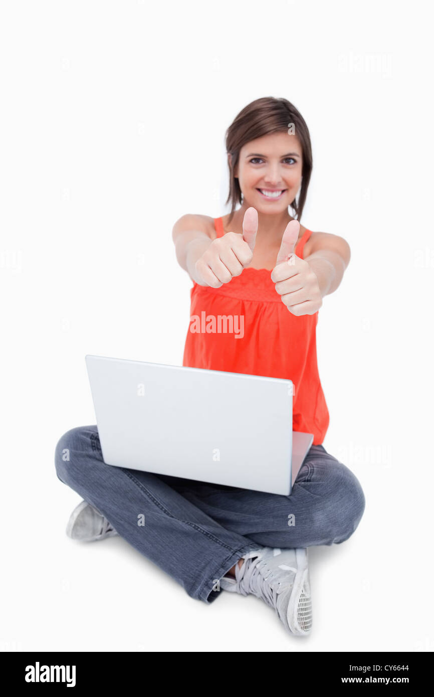 Teenage girl sitting cross-legged and showing her happiness by putting her thumbs up Stock Photo