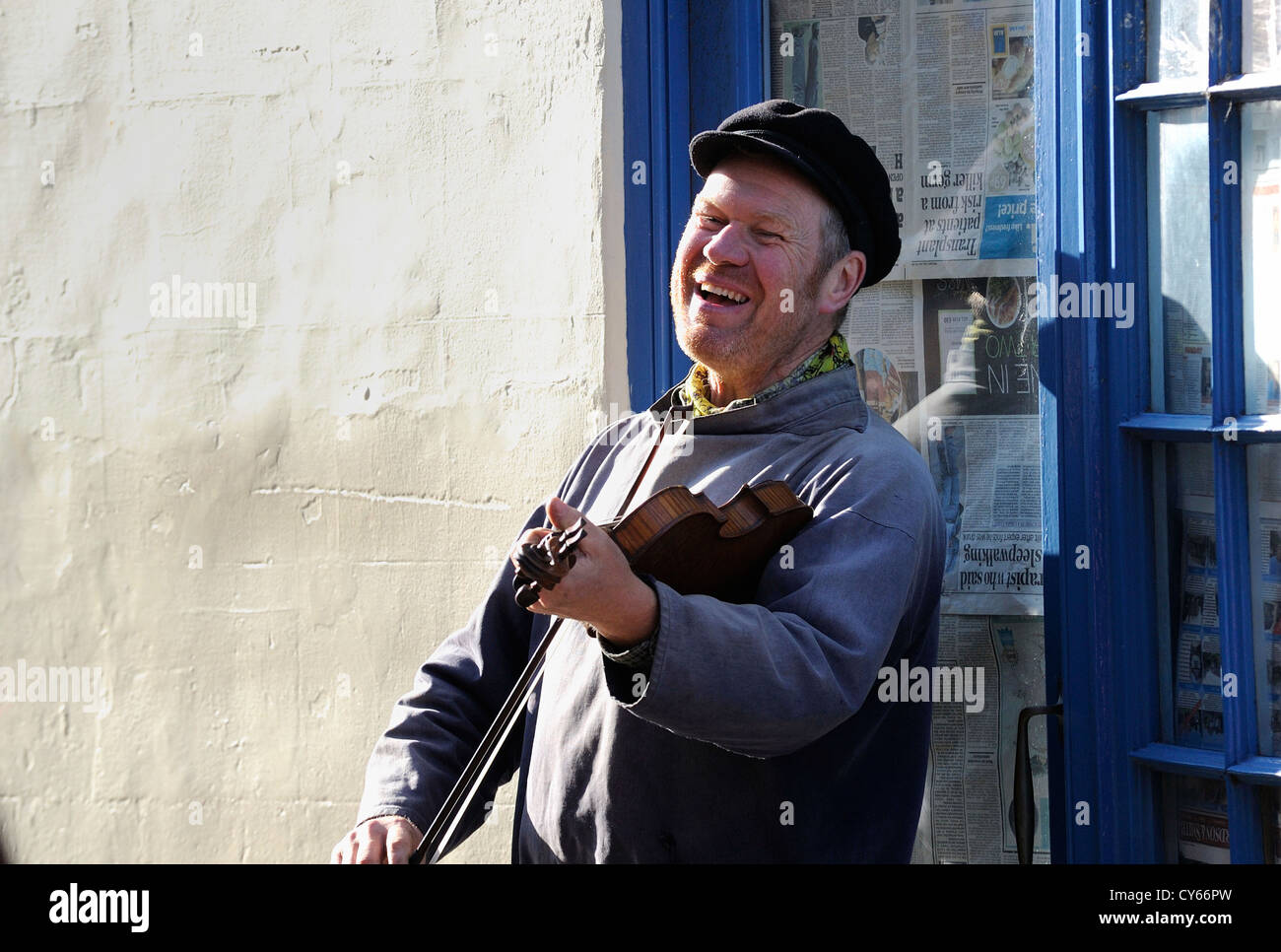 Street busker playing a musical instrument and entertaining the general public for money in the narrow streets on Whitby. Stock Photo