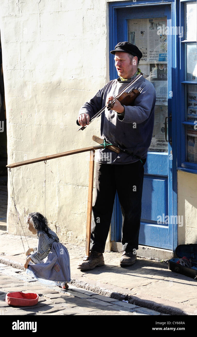 Street busker playing a musical instrument and entertaining the general public for money in the narrow streets on Whitby. Stock Photo