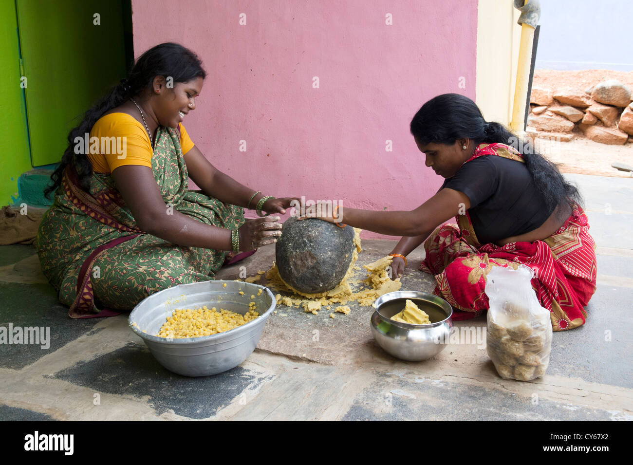 Indian women mixing Jaggery Dal mixture with a grinding stone for making Dasara festival sweets in a rural Indian village. India Stock Photo