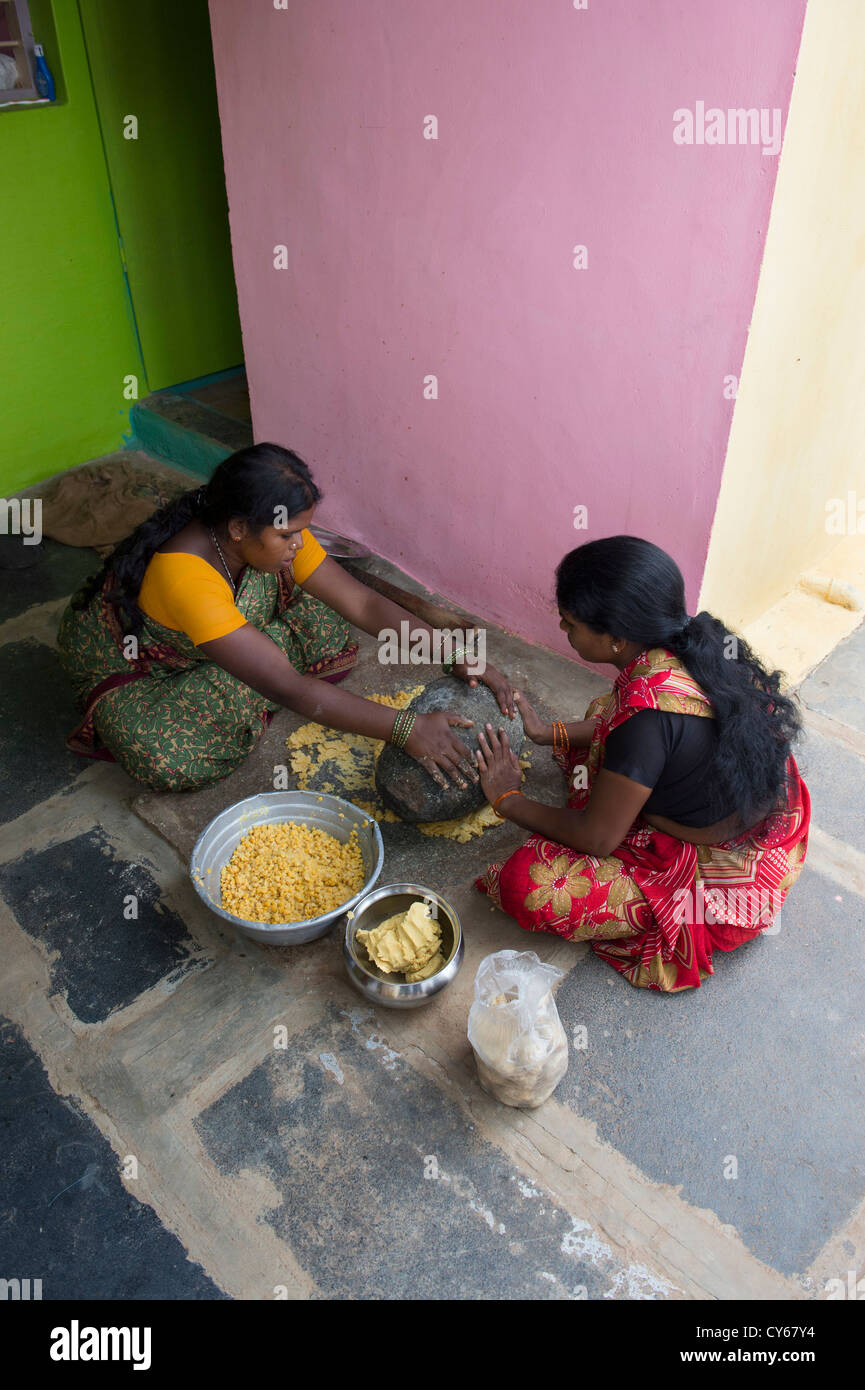 Indian women mixing Jaggery Dal mixture with a grinding stone for making Dasara festival sweets in a rural Indian village. India Stock Photo